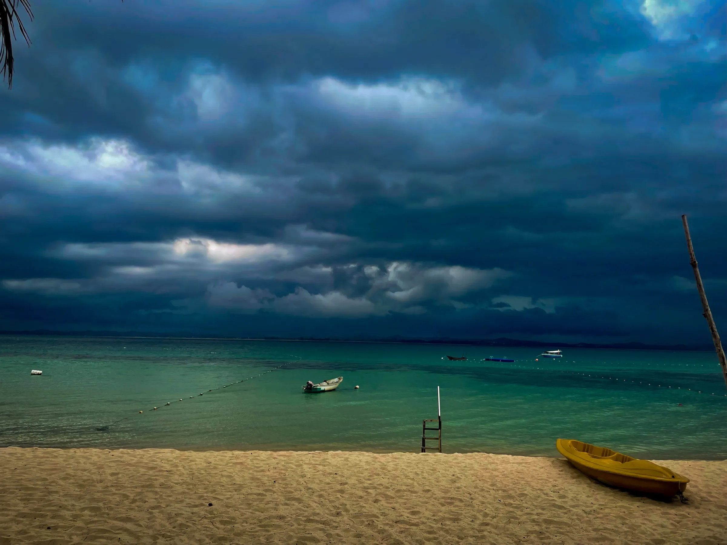 An empty beach and small yellow boat beneath an approaching storm