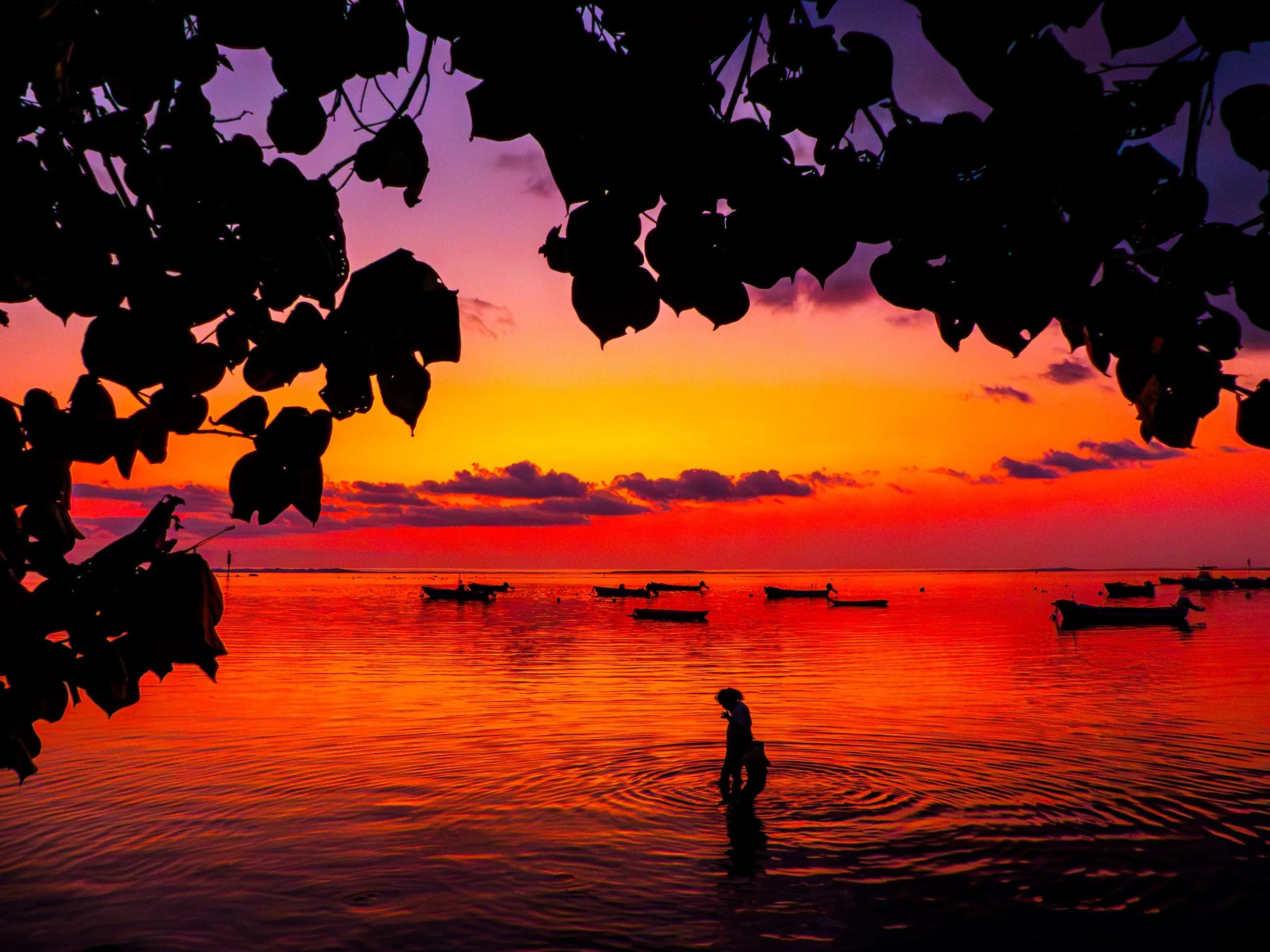 A lone figure in shallow water beneath a saturated sunset