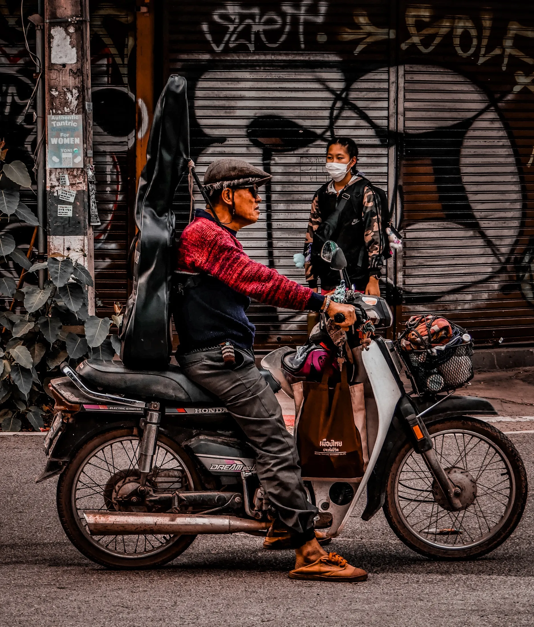 Two people pause beside a motorcycle on a city street