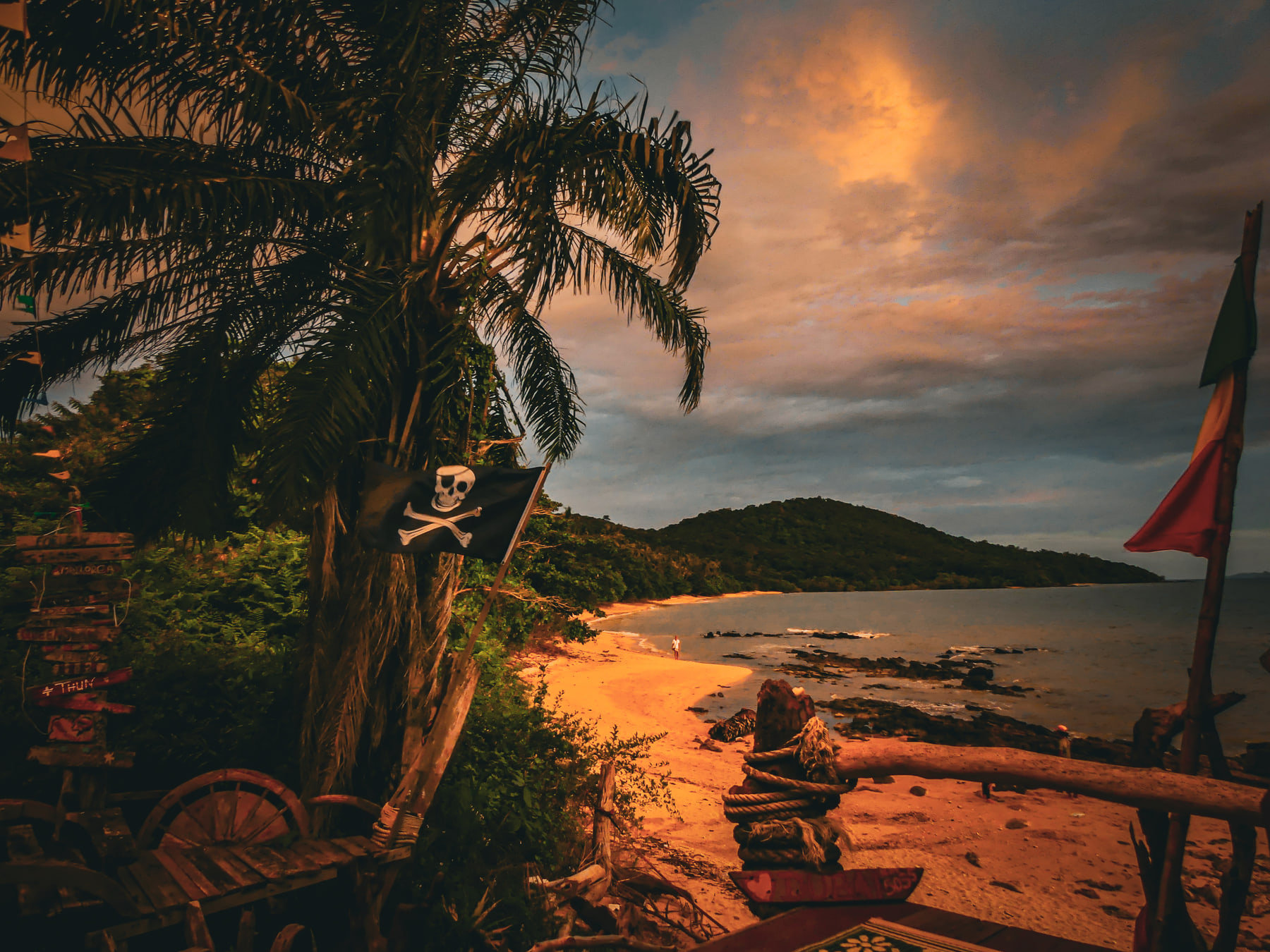 Palms lean over a beach at low tide with a long boat drawn up on the sand under warm cloud.