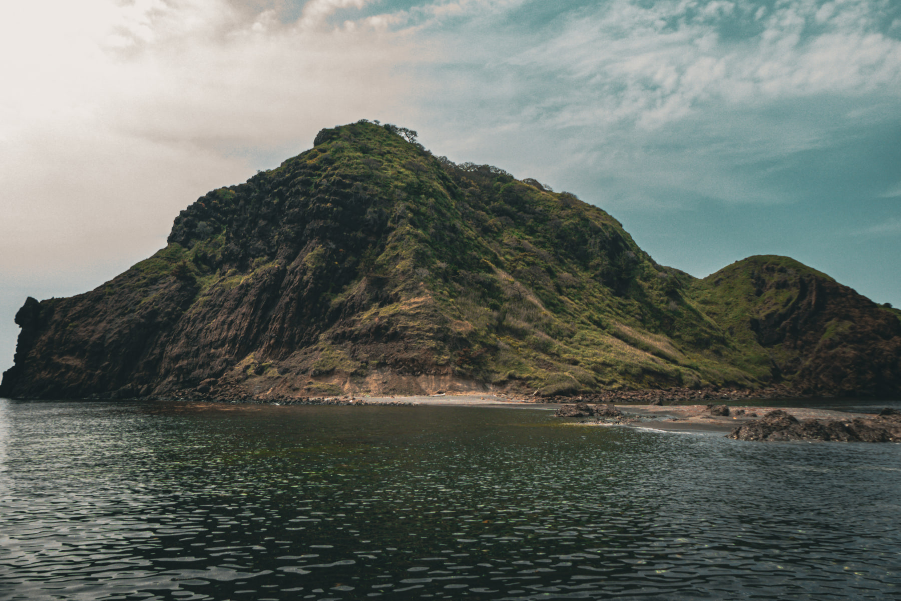 A steep green headland rises straight out of the sea beside a pale shingle beach.