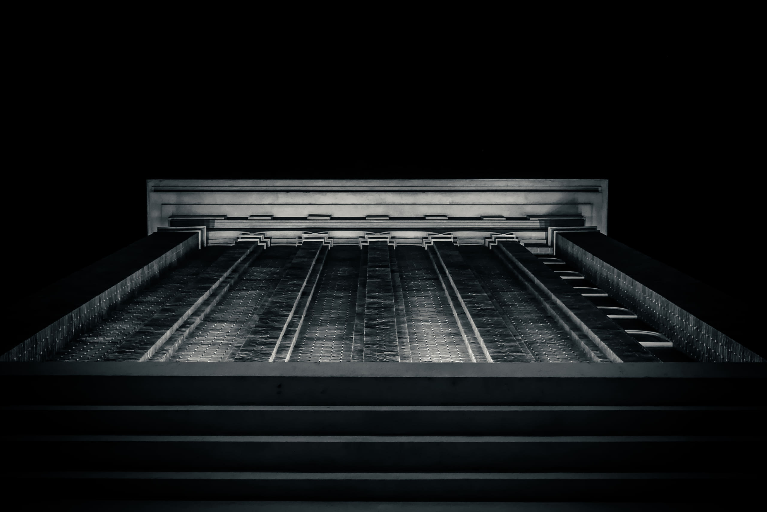 A tall, symmetrical building facade rises out of deep shadow against a black night sky.