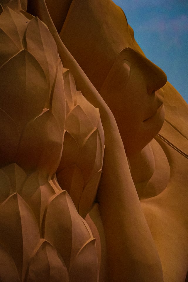 A carved face and lotus petals rise against blue sky.