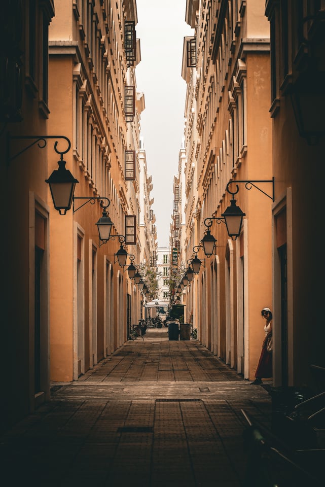 A narrow lane of tall buildings runs into the distance beneath hanging lamps.
