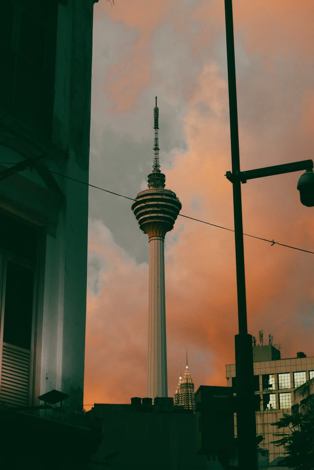A telecoms tower rises between buildings under orange cloud.