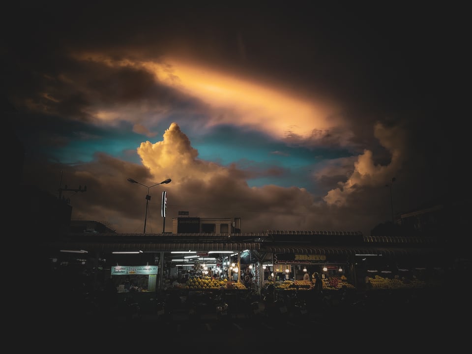 A lit market sits beneath a break of cloud at dusk.
