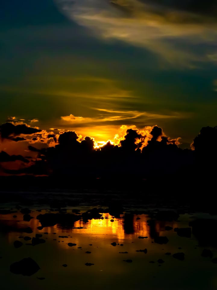 The sun burns through cloud above a flooded shore.