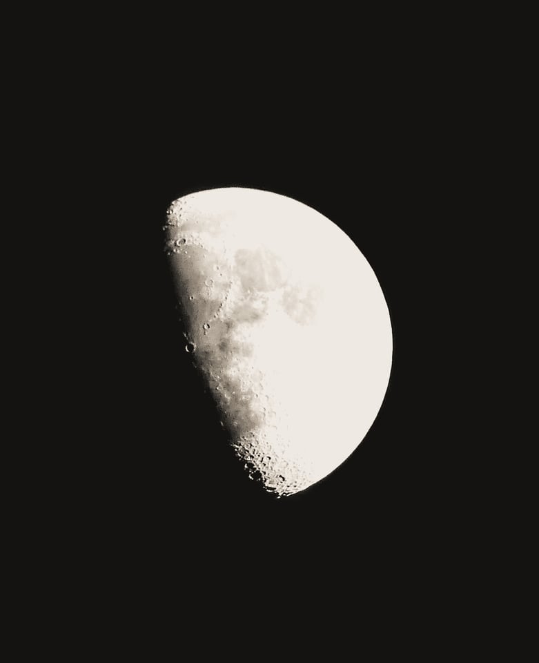 A half moon shows its craters in fine detail against black.