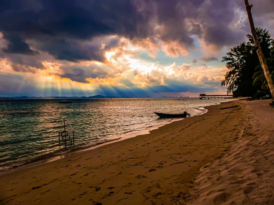Sunbeams break through cloud over a beach with a moored boat.