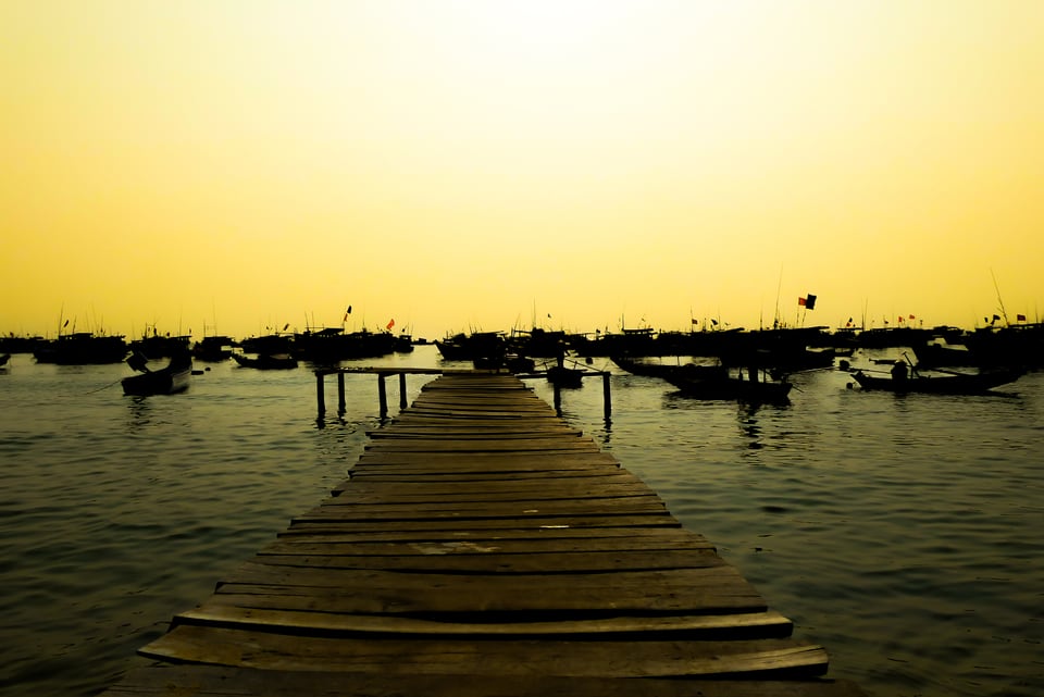 A wooden jetty runs out to moored boats under a yellow sky.