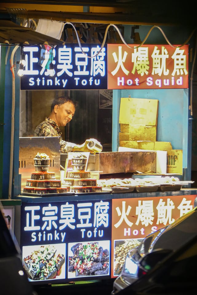 A vendor stacks food behind the counter of a brightly lit stall.