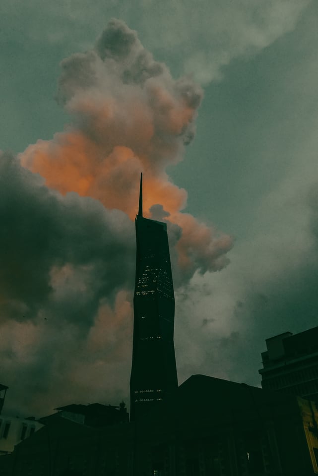 A tall spired tower stands in cloud above a city skyline.