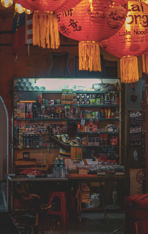 A small hardware stall glows beneath red paper lanterns.