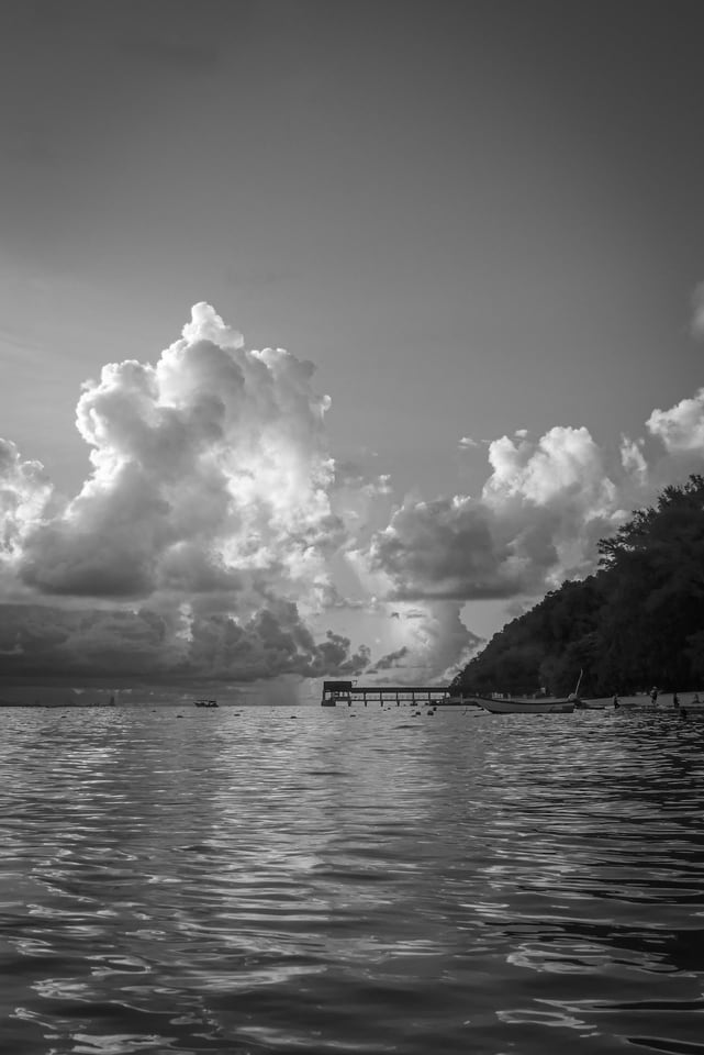 Cloud stacks above a bay with a pier and moored boats.