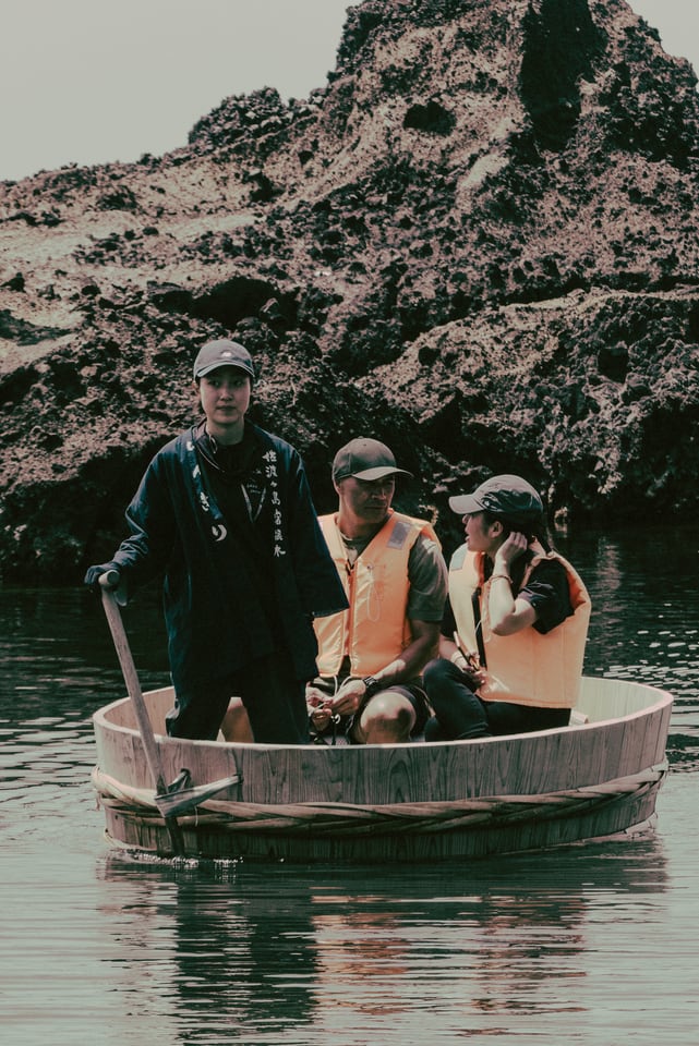 Three people cross still water in a small round boat.