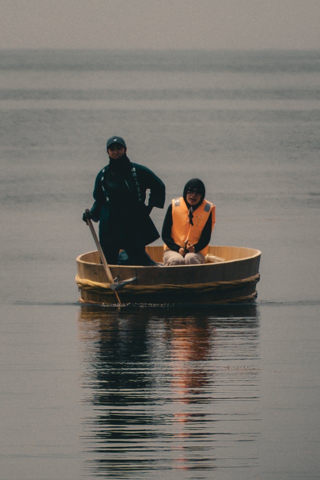 Two people travel across still water in a small round boat.
