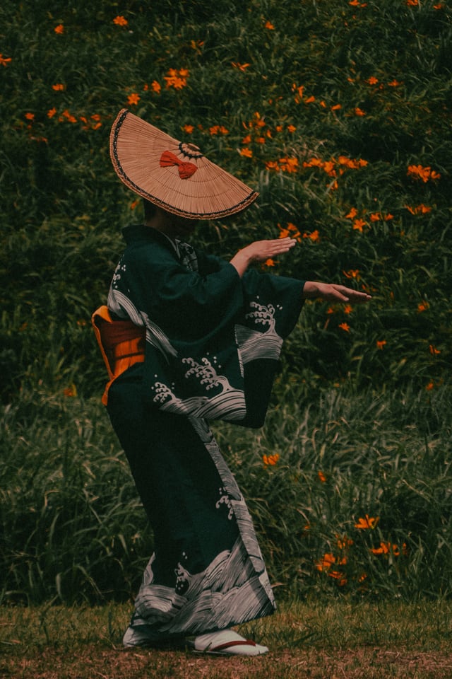 A dancer in a straw hat turns mid-step in front of orange flowers.