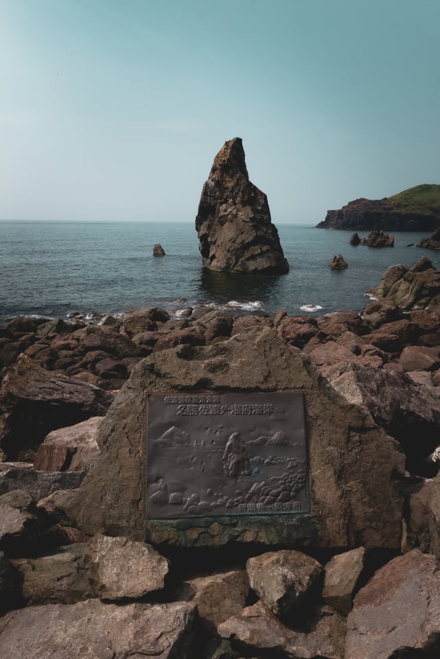 A tall sea stack rises beyond a shore of pale boulders.