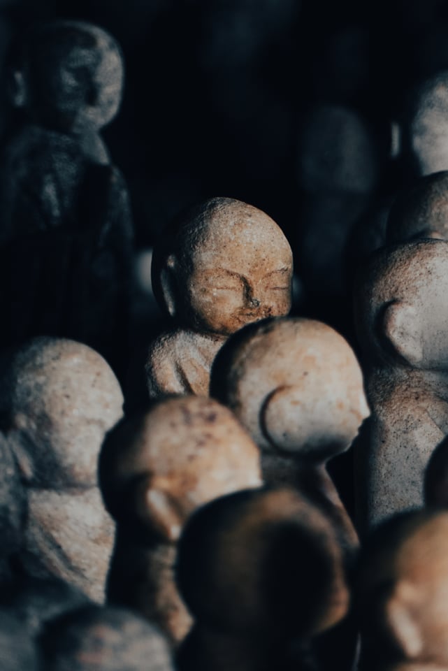 Rows of small weathered stone figures stand crowded together in low light.