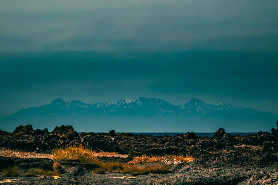 A teal sea runs out towards a distant range of snow-covered mountains.