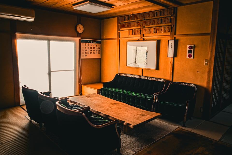 Low evening light crosses a tatami room with dark seating.