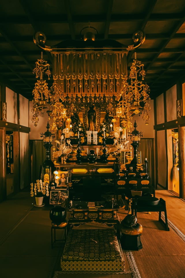 A gilded altar stands at the end of a dim tatami hall, a mat and low stands laid out in front of it.