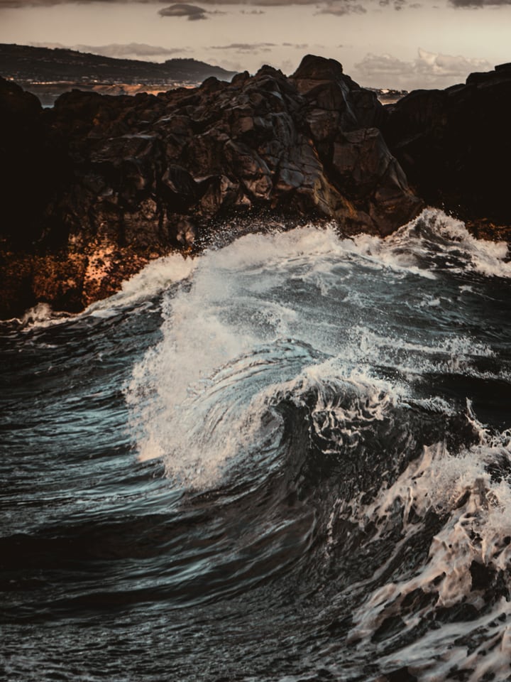 A wave folds over itself against black volcanic rock.
