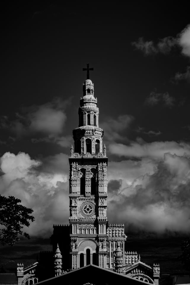 A pale church spire and its clock face against a bank of cloud.