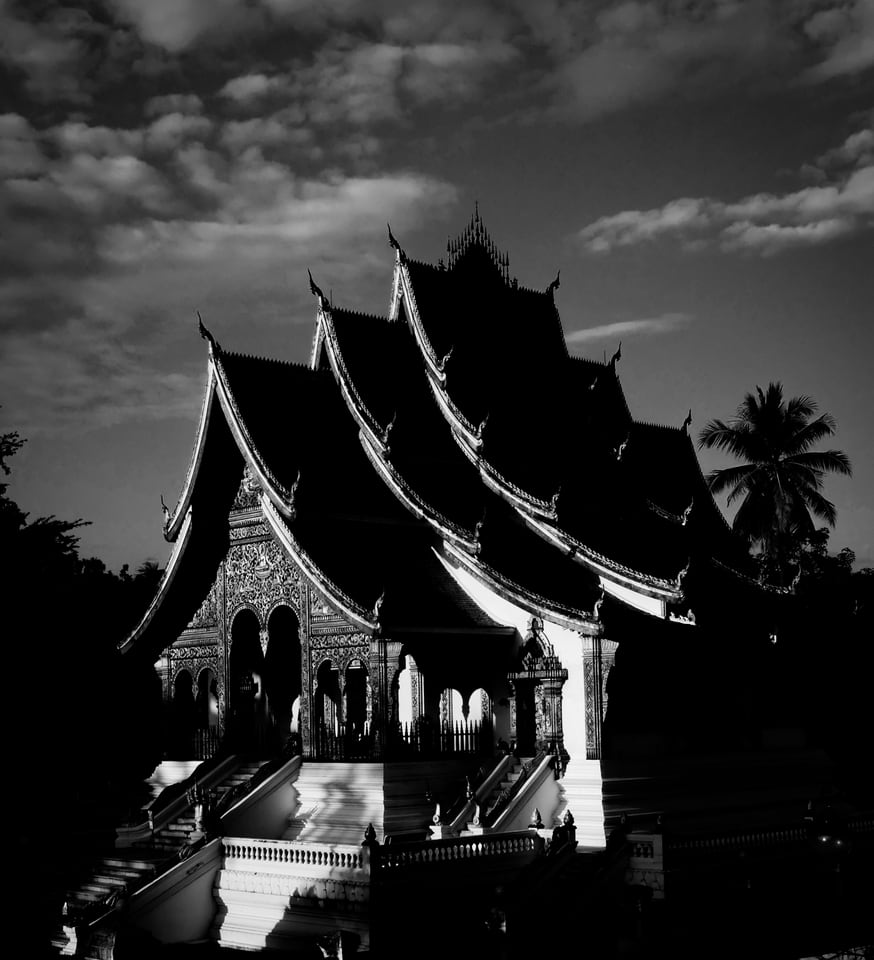 A many-tiered temple roof stands in deep shadow beneath a sky filled with textured cloud, rendered in black and white.