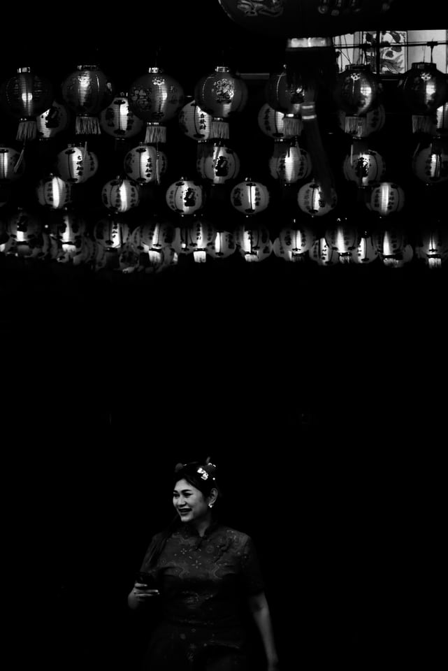 Rows of paper lanterns hang above a woman in a dark street.