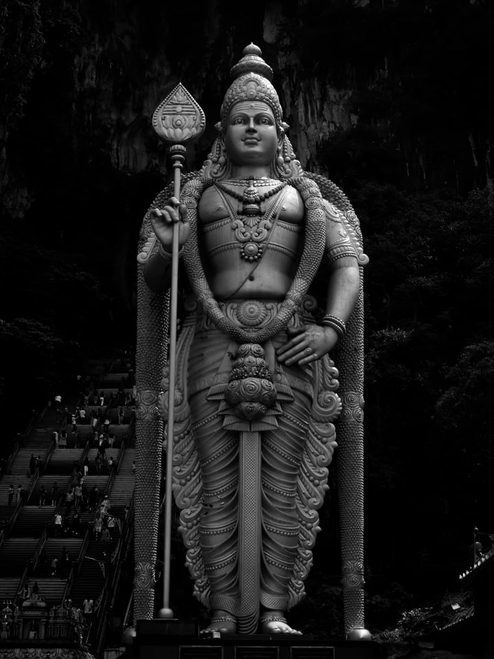 A tall statue of a standing deity holding a spear, in black and white, above a flight of steps.