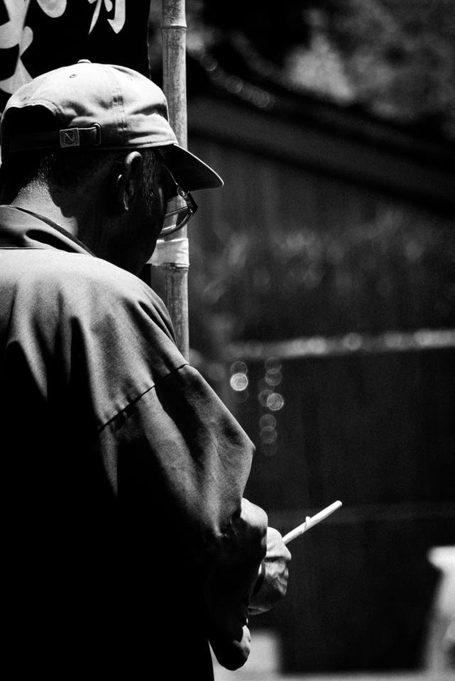 A man in a cap holds a cigarette at the edge of a doorway.