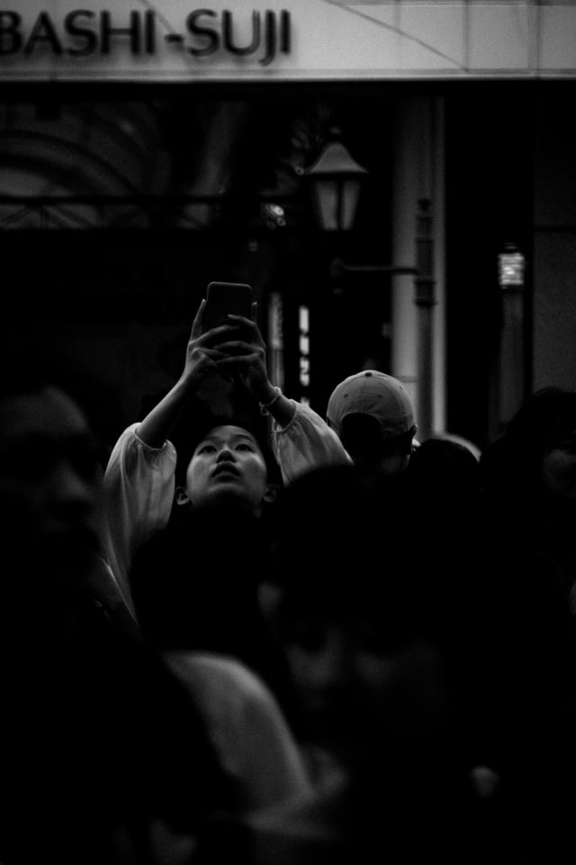 A phone is raised above a crowd beneath an arcade sign.