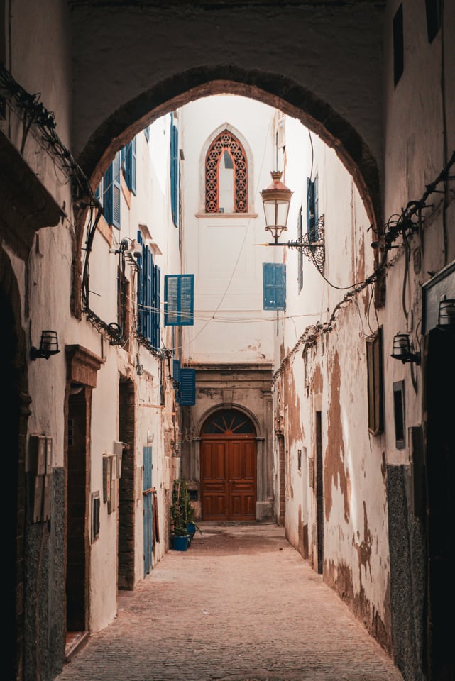A vaulted passage opens onto a lane, with lanterns along the wall.