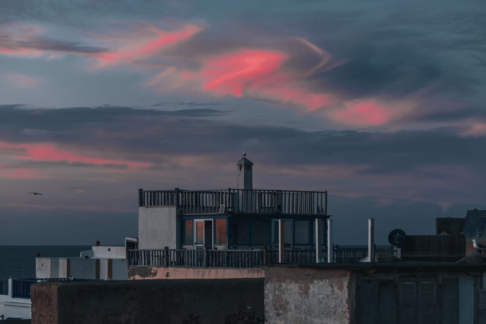 Pink and violet dusk over a rooftop terrace with the sea behind.