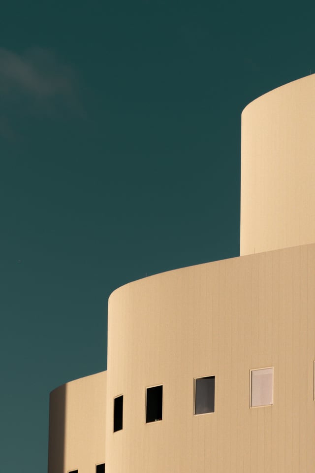 Two pale curved walls step against an empty teal sky.