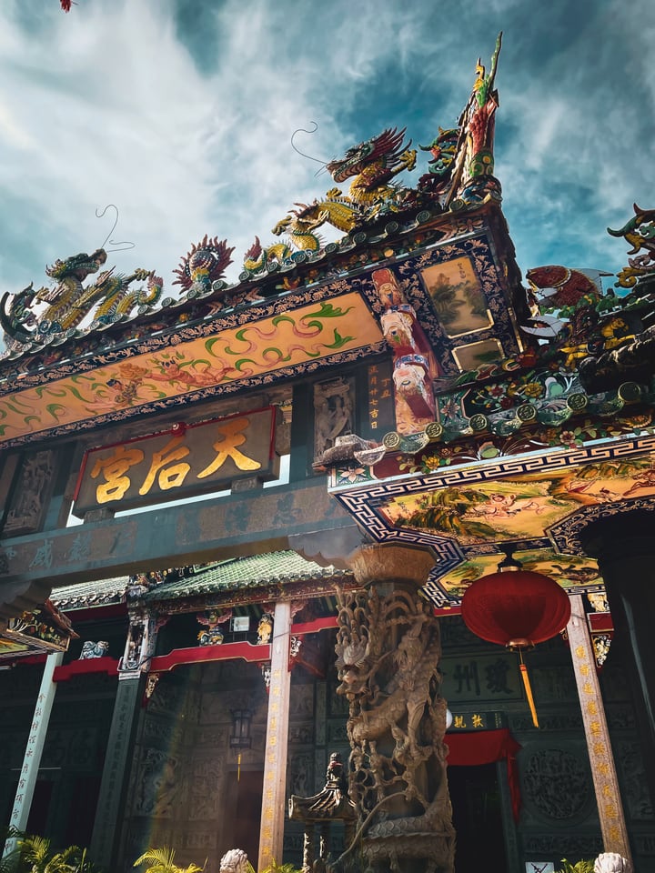 The roof of a Chinese temple seen from below, crowded with painted dragons, above a carved stone pillar and a red lantern.