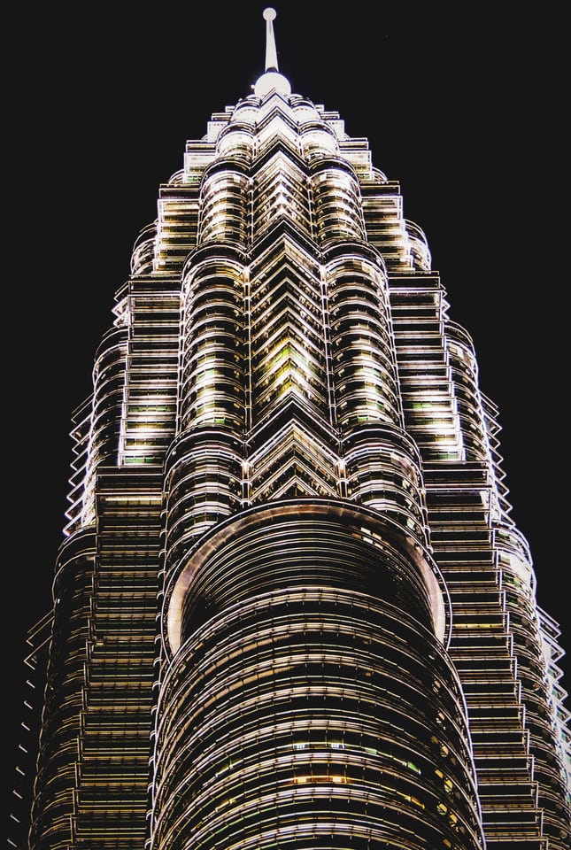 The upper section and spire of a skyscraper at night, seen from directly below, its stepped tiers lit against a black sky.