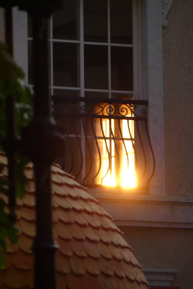 Late sunlight glows through a decorative balcony window above overlapping tiled roofs.